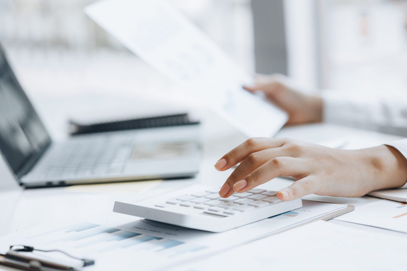 A desk mid-close: calculator, printed reports and a laptop